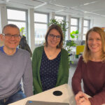Michael Gerwinat, Maria Schmalenbach und Mareike Weber sitzen in den Räumlichkeiten der Projektwerkstatt und lächeln freundlich in die Kamera.