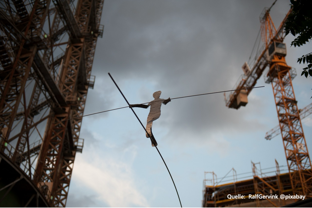 Ein Seiltänzer aus Pappe balanciert über eine schmale Stange am Gasometer Berlin.