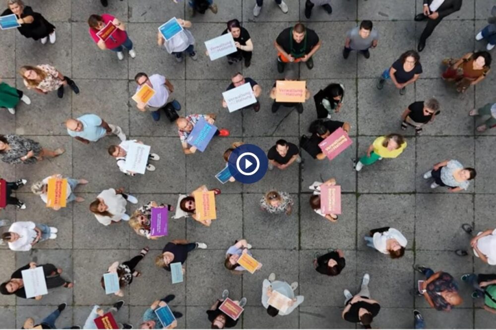 Das von oben aufgenommene Foto zeigt viele Mitarbeitende auf dem Hof am Rathaus, viele von Ihnen halten große Schilder in verschiedenen Farben mit der Aufschrift "Verwaltung mit Haltung".