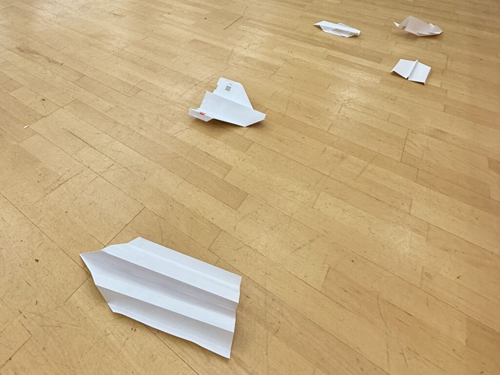 Auf dem Fußboden der VHS liegen verstreut verschiedene gelandete Papierflieger.